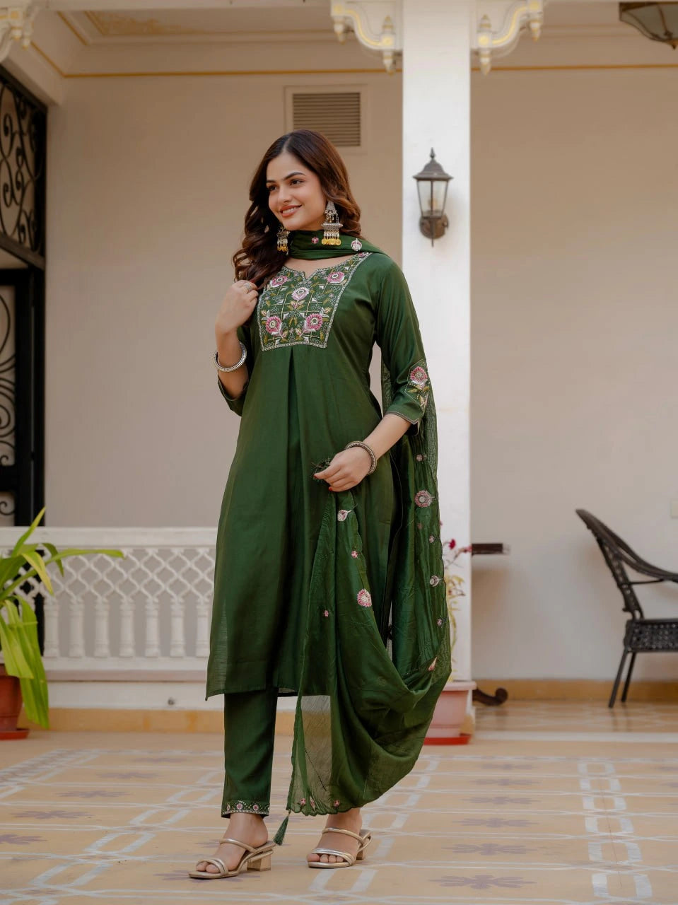 Woman wearing a green traditional outfit with floral embroidery in an indoor setting.