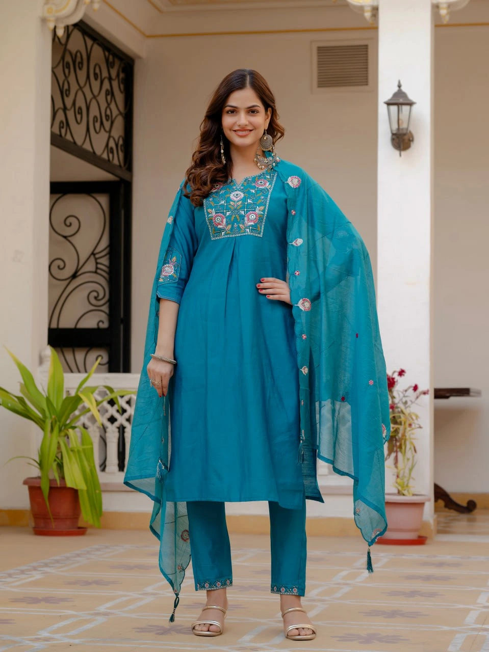 Woman in a teal traditional outfit with floral embroidery indoors.
