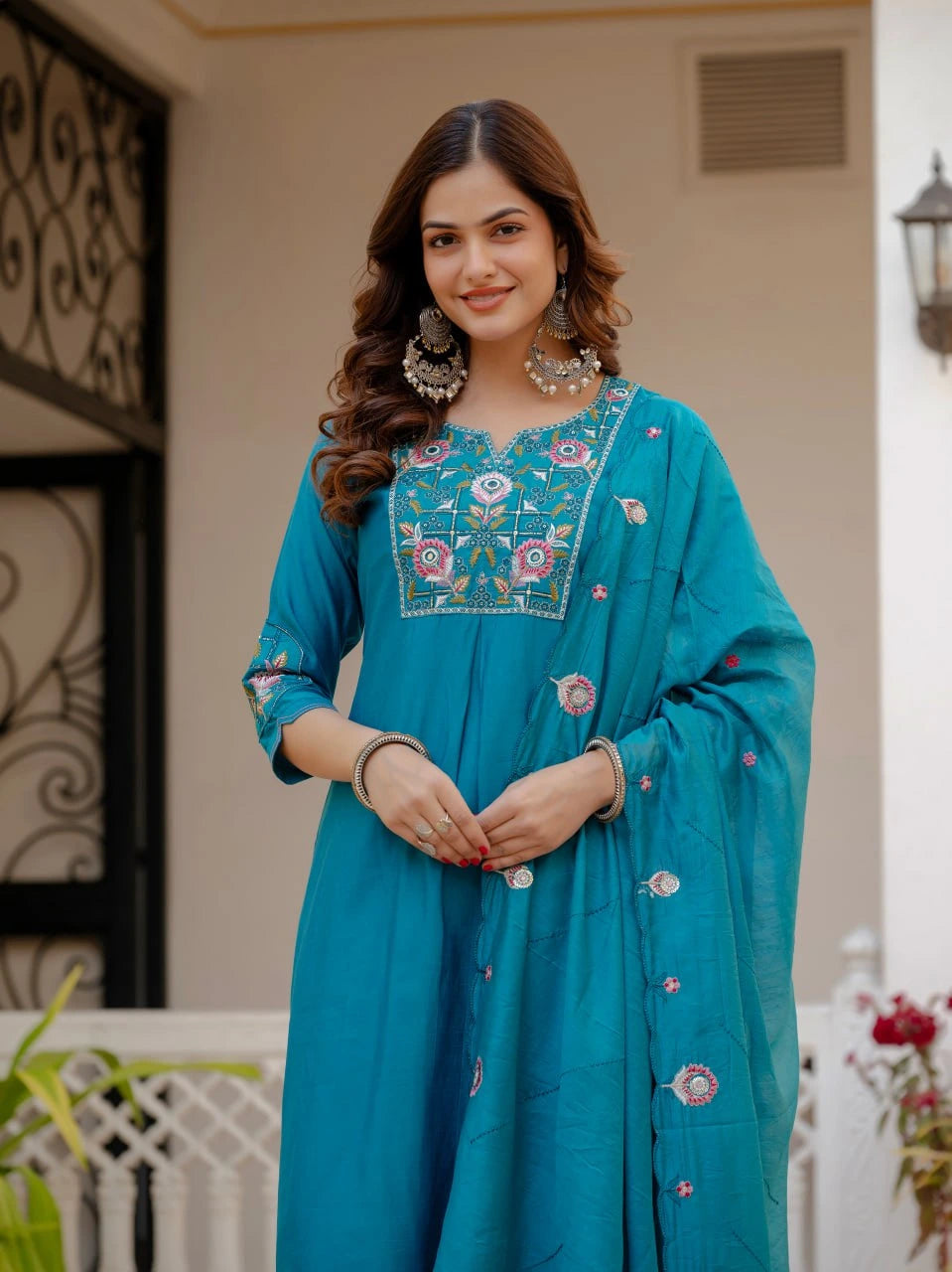 Woman wearing a teal embroidered traditional outfit standing outdoors.