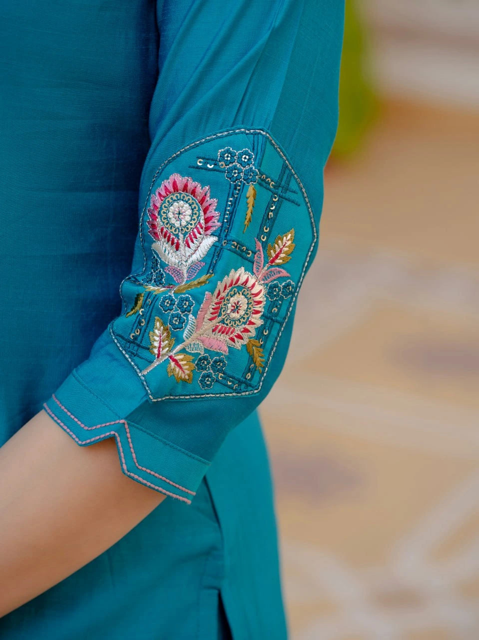 Close-up of a teal sleeve with intricate floral embroidery on a blurred background