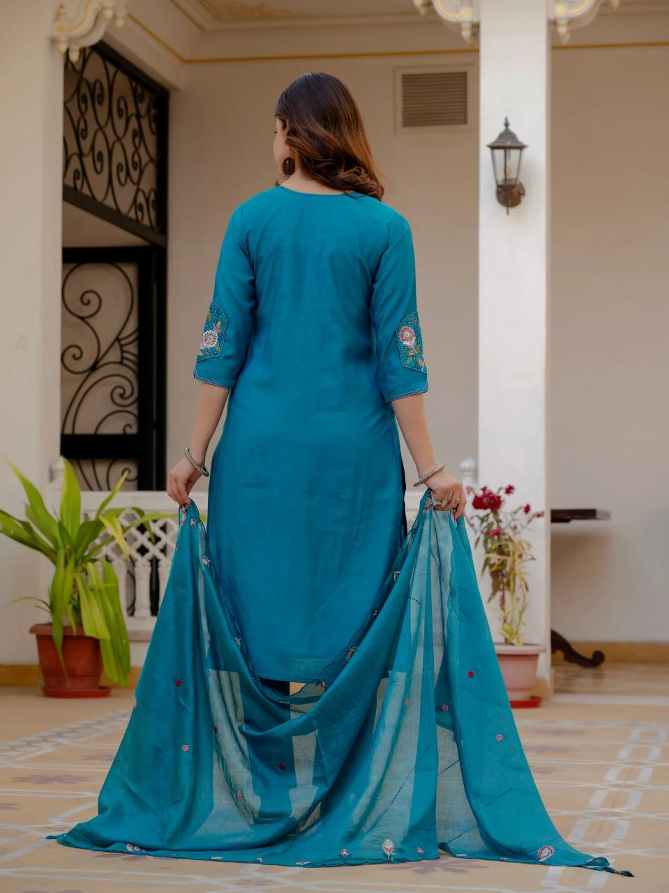 Woman in a blue traditional outfit holding a matching dupatta in an indoor setting.