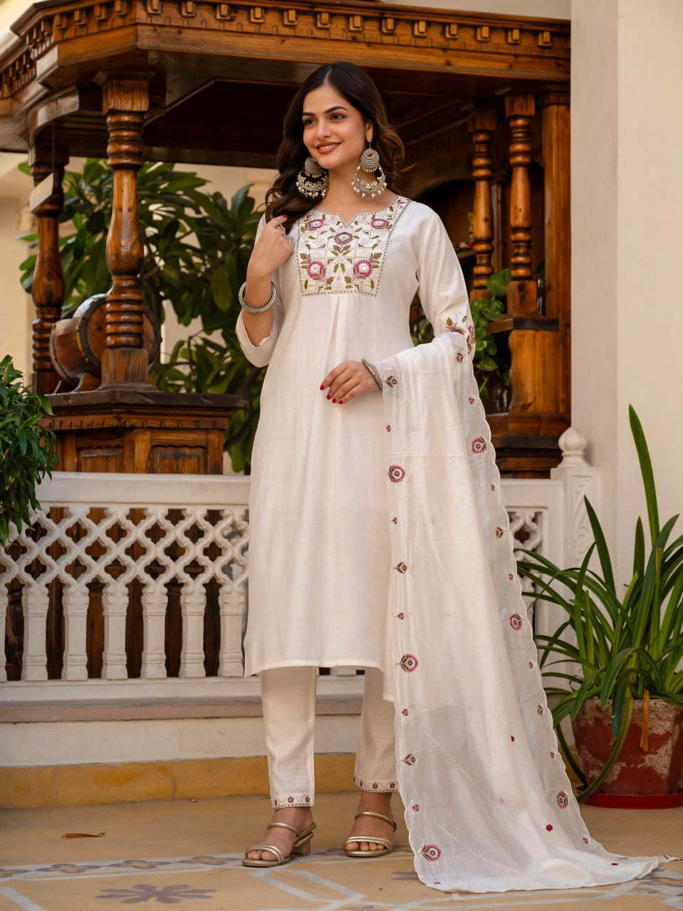 Woman in a white embroidered outfit standing in an ornate indoor setting.