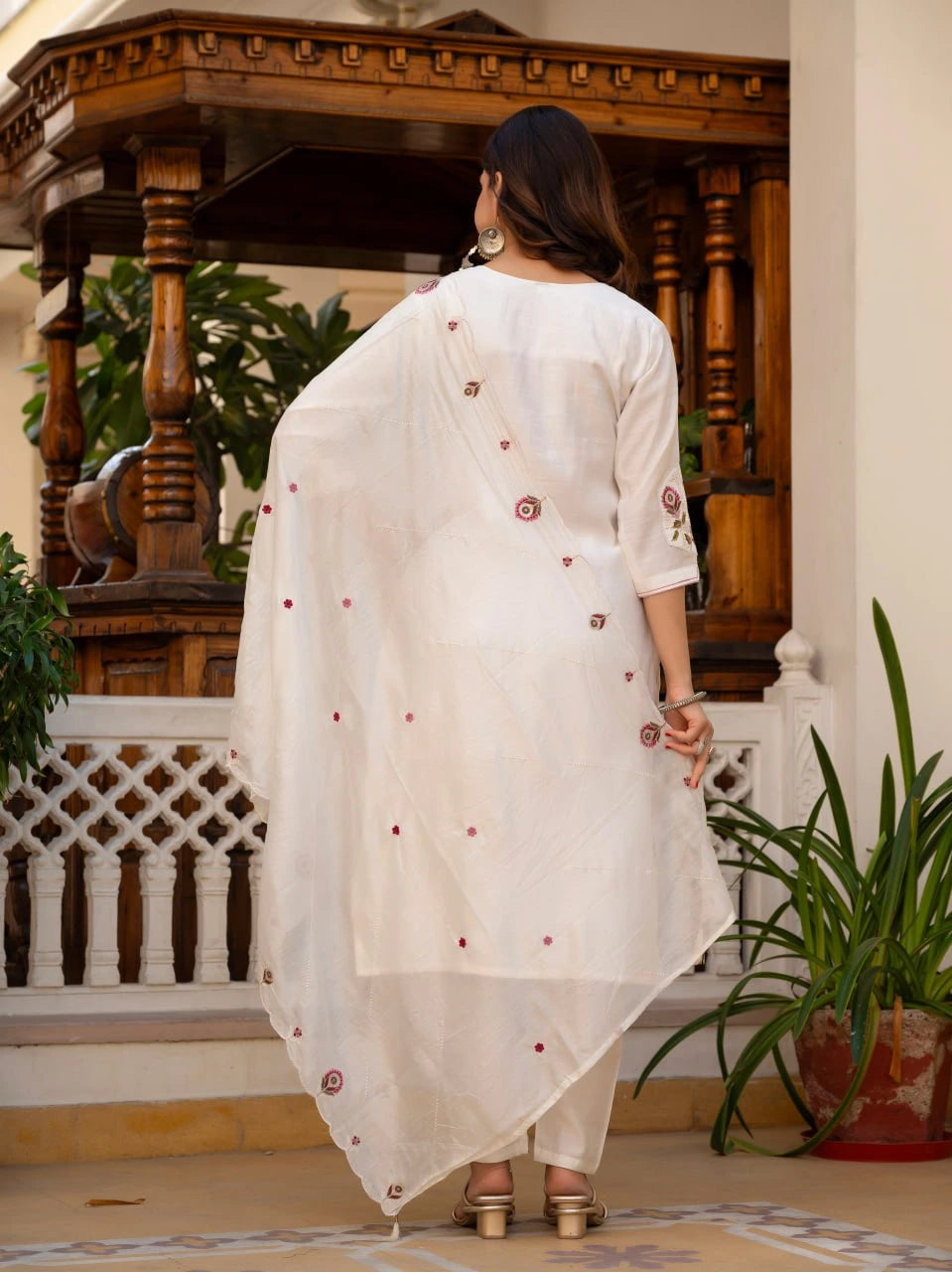 Woman wearing a white embroidered dupatta in an indoor setting with wooden architecture and plants.