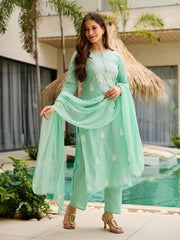 Woman in a light green traditional outfit standing by a pool with plants in the background