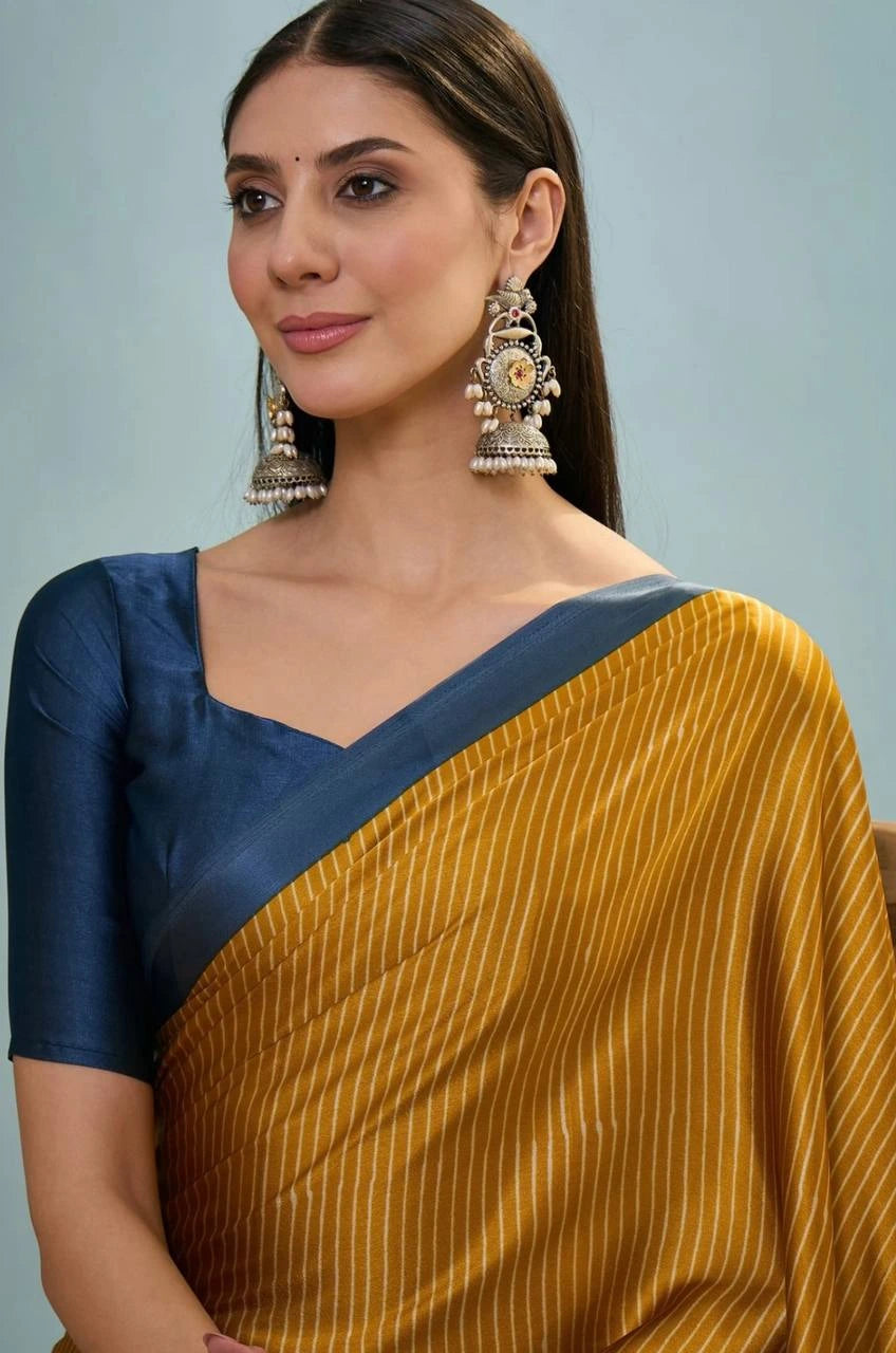 Woman wearing a yellow saree with a blue border and large earrings against a light gray background