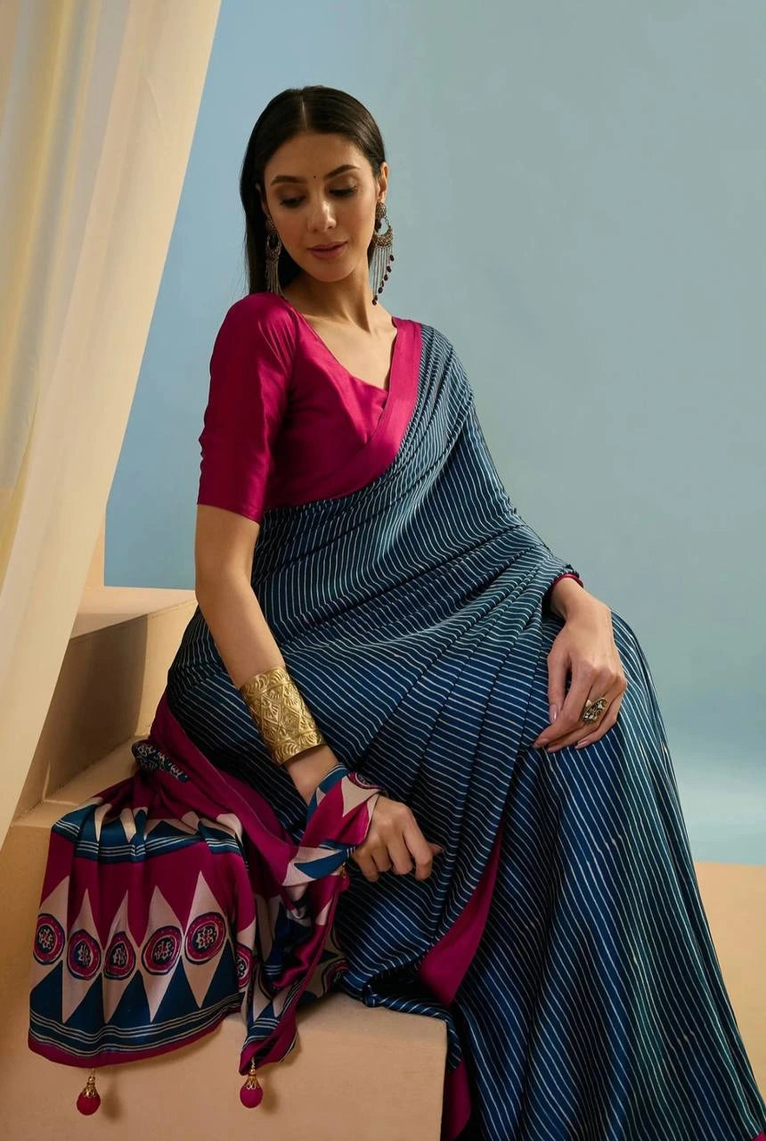 Woman in a blue saree with a pink blouse sitting on a bench against a light blue wall.