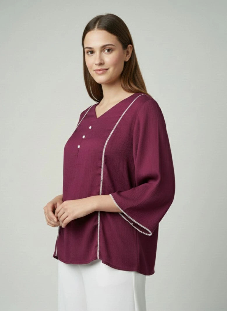 Woman wearing a burgundy top with white piping on a plain background