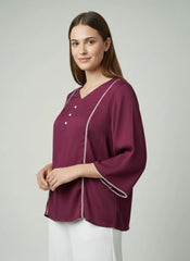 Woman wearing a burgundy top with white piping on a plain background