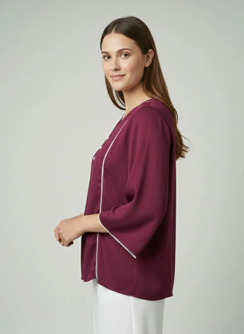 Woman wearing a burgundy top with a white trim on a plain background