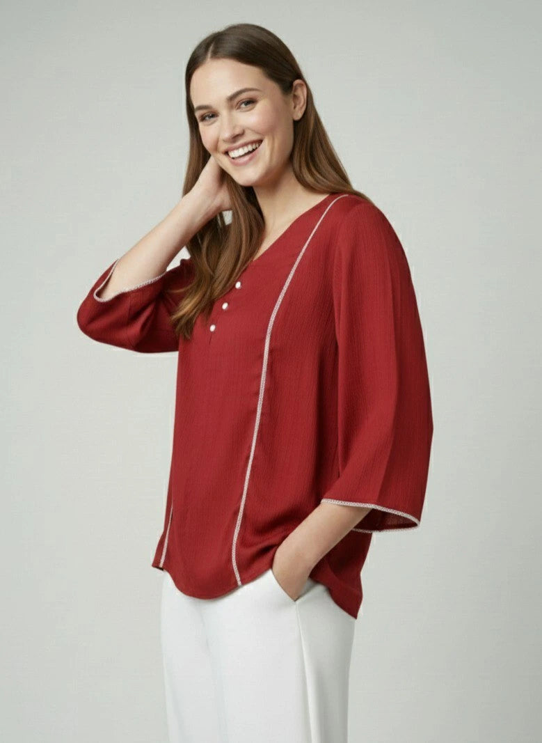 Woman wearing a red blouse with white trim on a plain background
