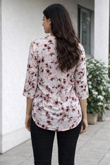 Woman wearing a floral blouse and black pants standing outdoors.