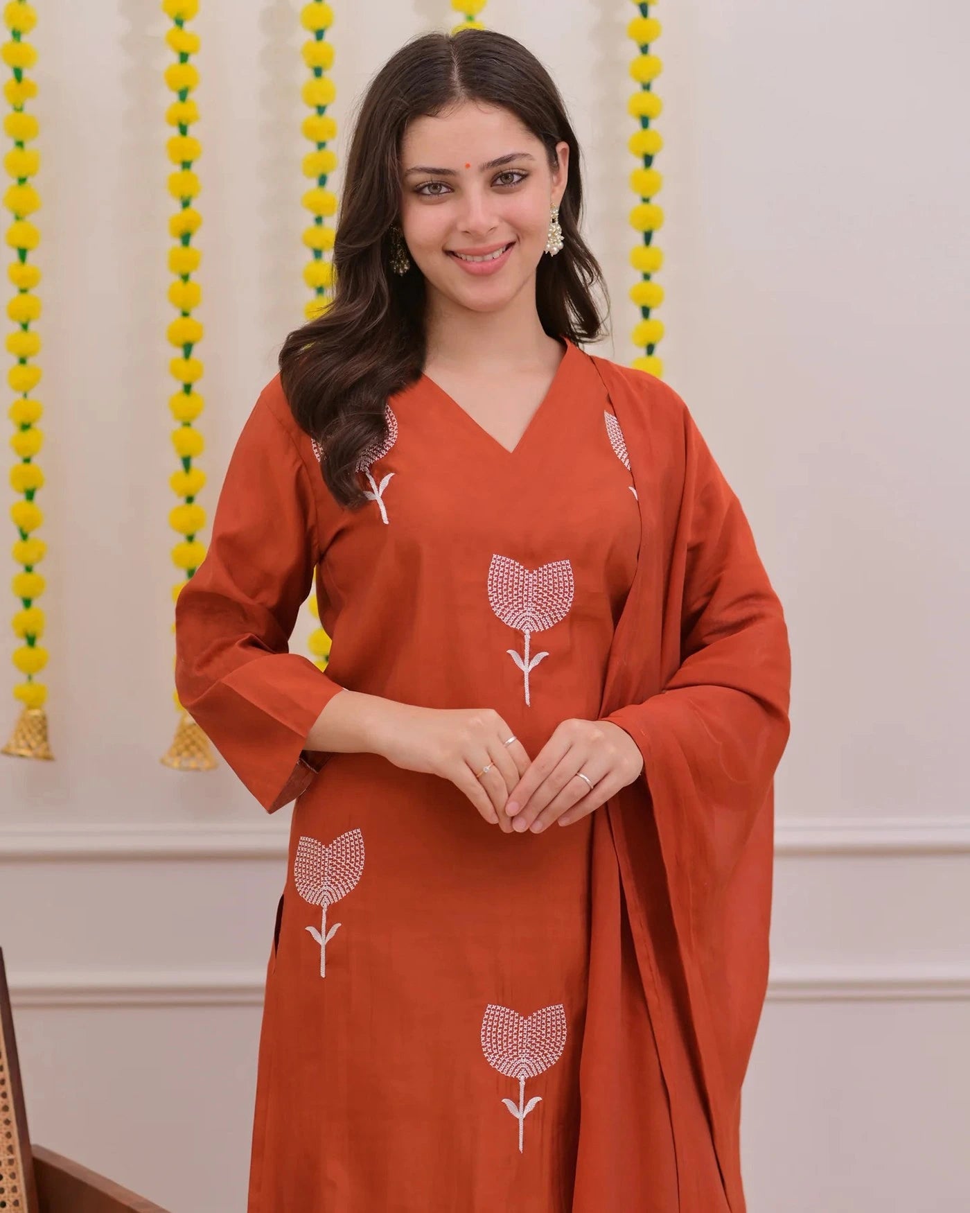 Woman wearing a rust-colored outfit with floral patterns against a decorative background