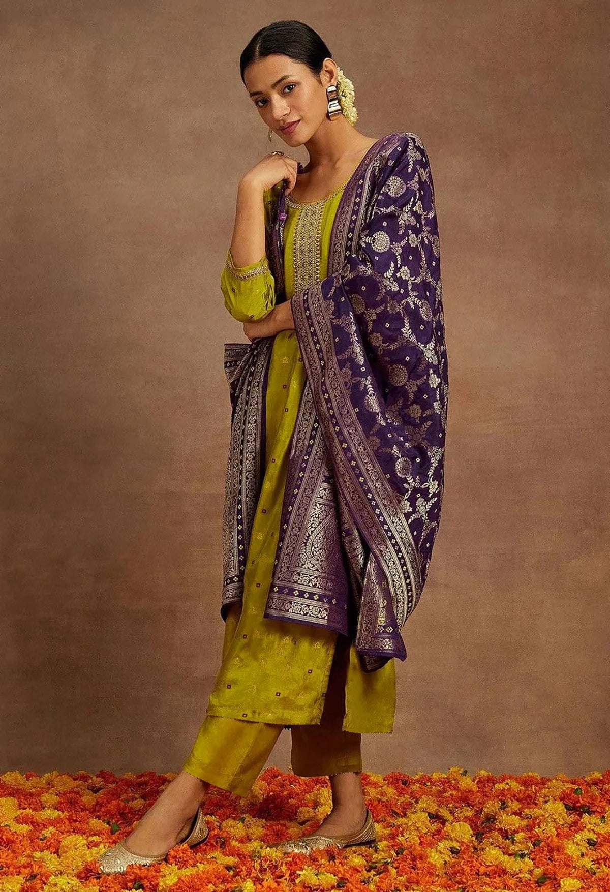 Woman in a yellow and purple traditional outfit standing on a floral ground with a brown background
