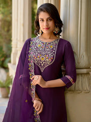 Woman wearing a purple embroidered outfit standing against a decorative column.