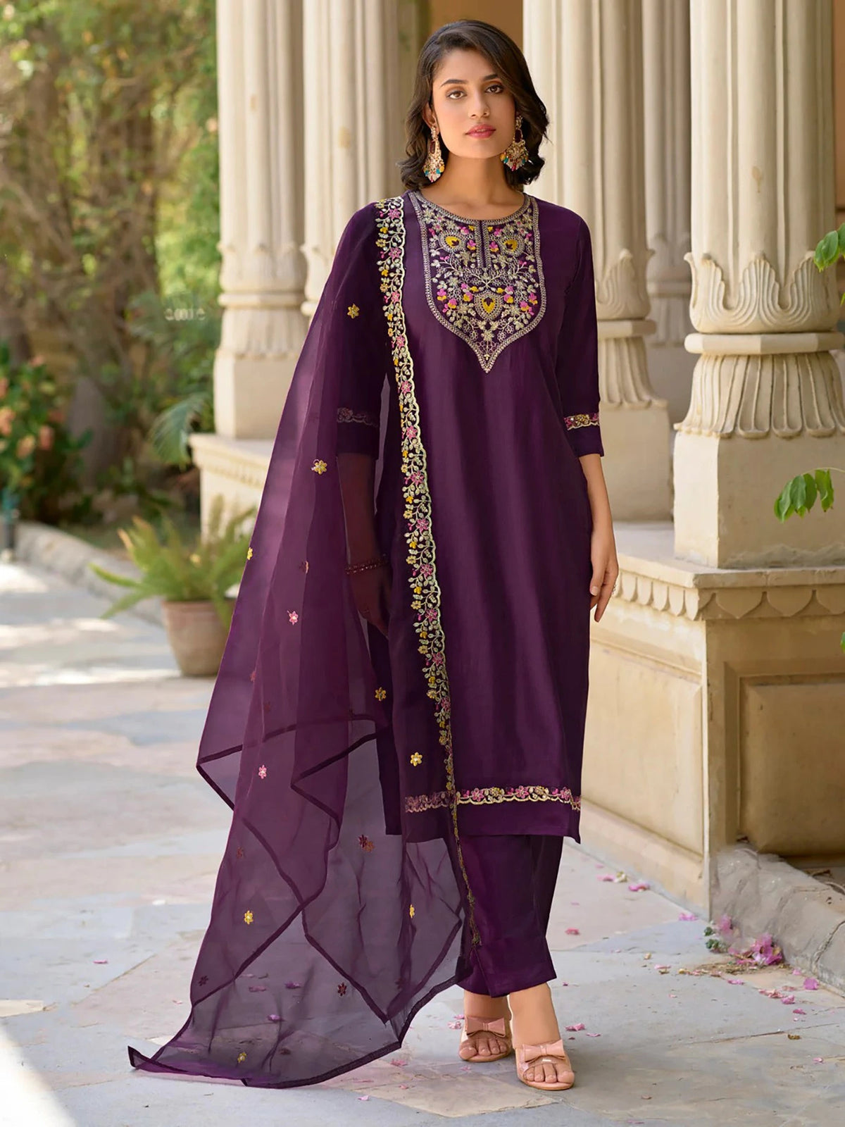 Woman in a traditional purple outfit with intricate embroidery standing outdoors.