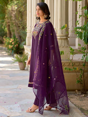 Woman in a purple traditional outfit with embroidery standing outdoors.