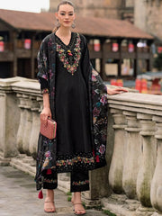 Woman in a black dress with floral embroidery standing on a stone bridge.