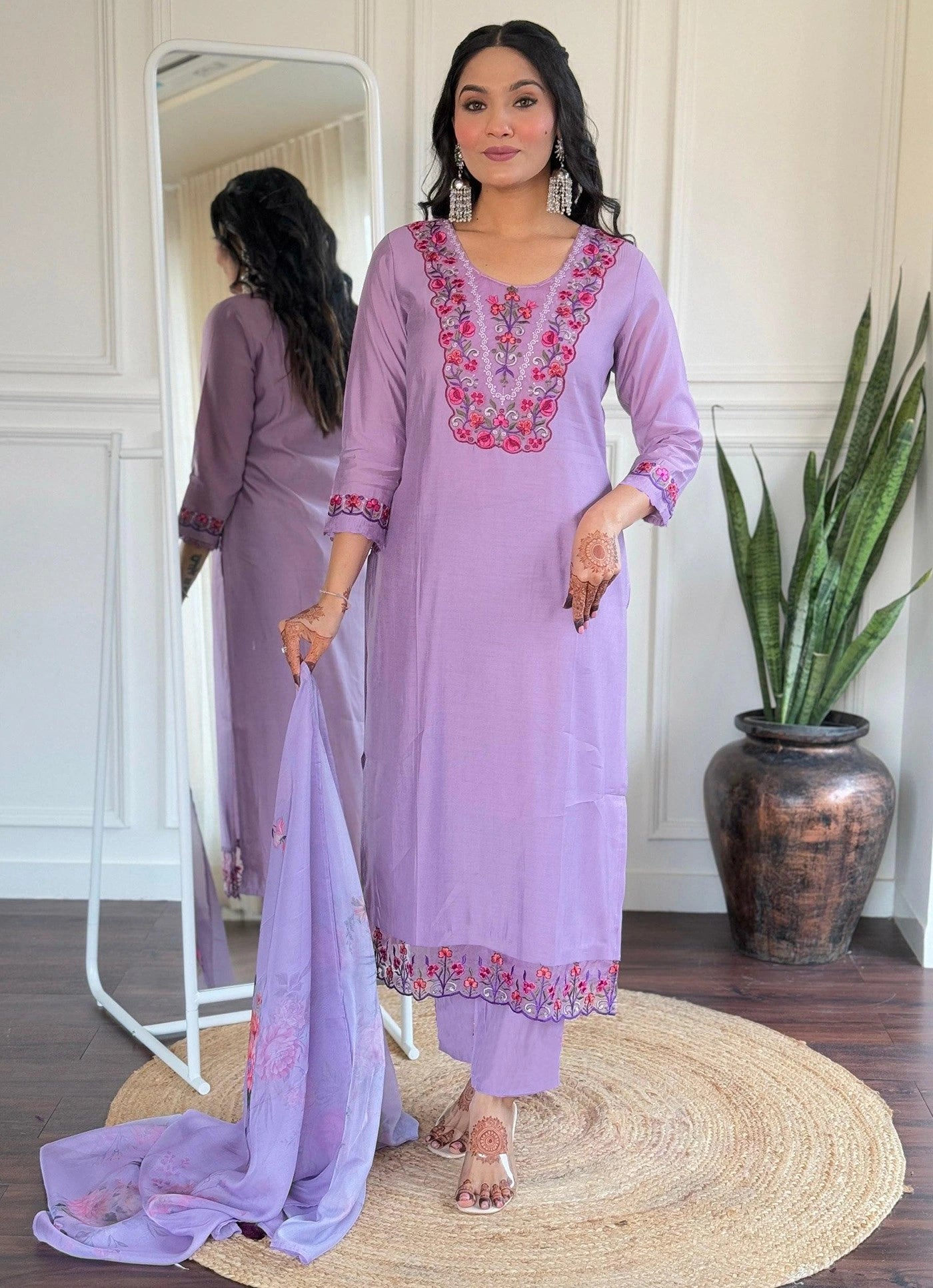 Woman in a lavender traditional outfit with pink embroidery standing in a room.