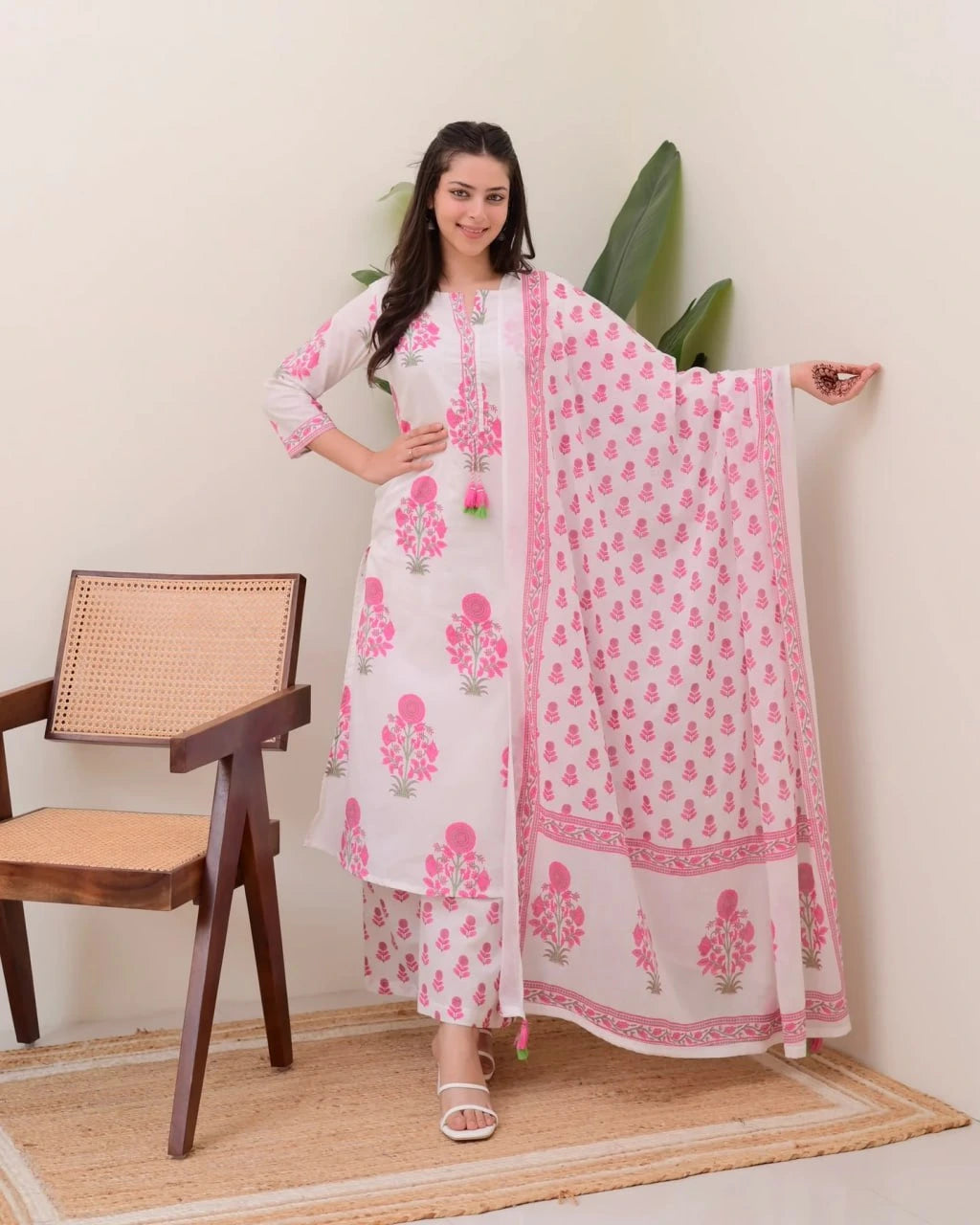 Woman wearing a white and pink traditional outfit with a matching dupatta in a room.