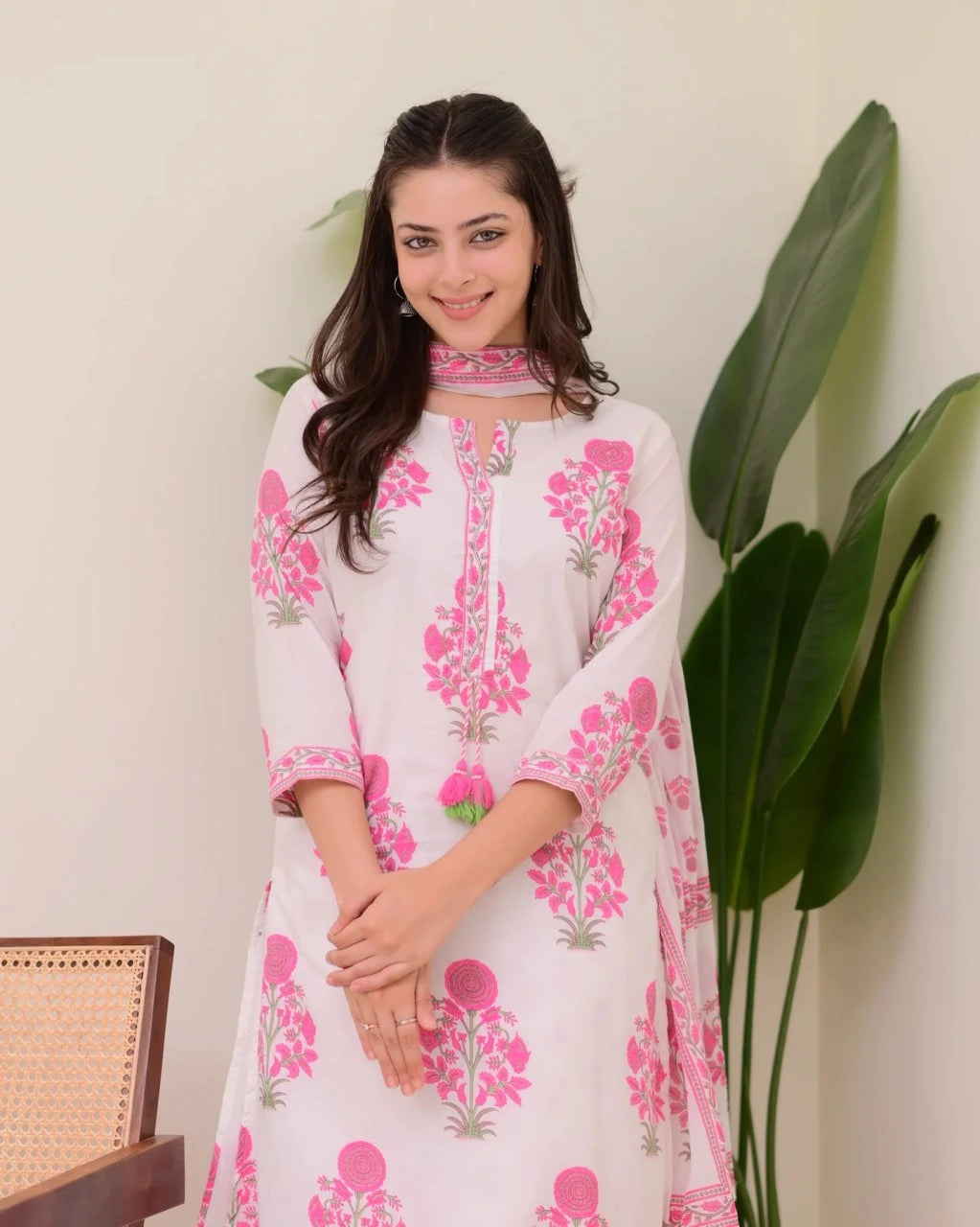 Woman wearing a white dress with pink floral patterns against a neutral background