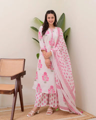 Woman wearing a white and pink floral outfit with a chair and plant in the background