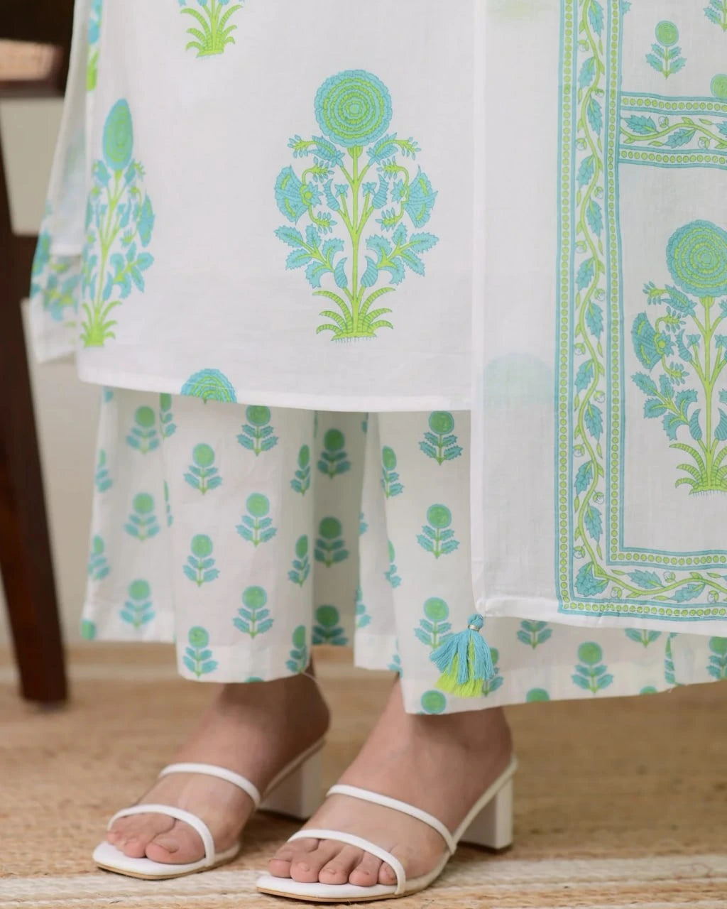 White outfit with green floral patterns and white sandals on a wooden floor.