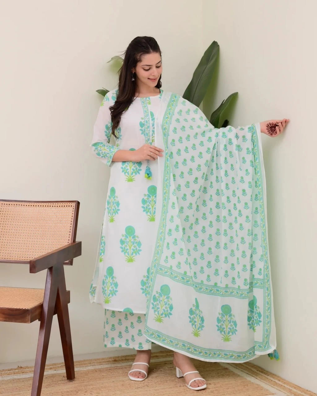 Woman wearing a white and green traditional outfit with a pattern, standing indoors.