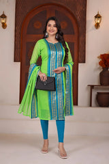 Woman in a green and blue traditional outfit holding a black clutch in a decorated room.