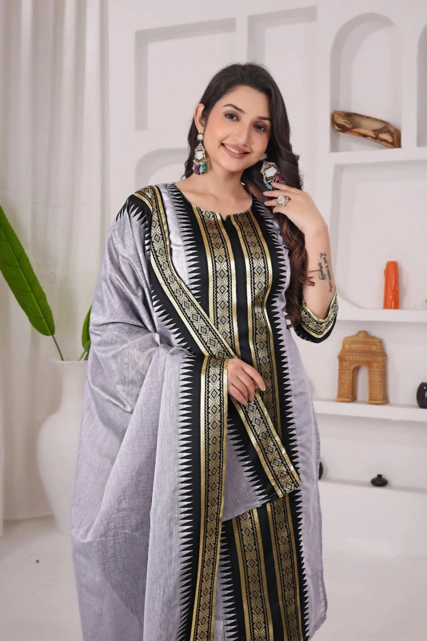 Woman wearing a gray saree with black and gold patterns in a minimalistic room.