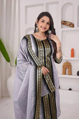 Woman wearing a gray saree with black and gold patterns in a minimalistic room.