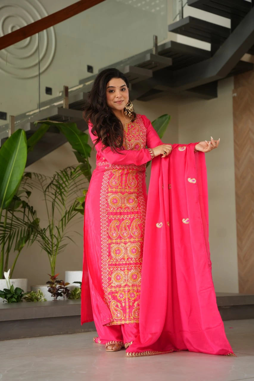 Woman in a bright pink traditional outfit with gold patterns indoors.