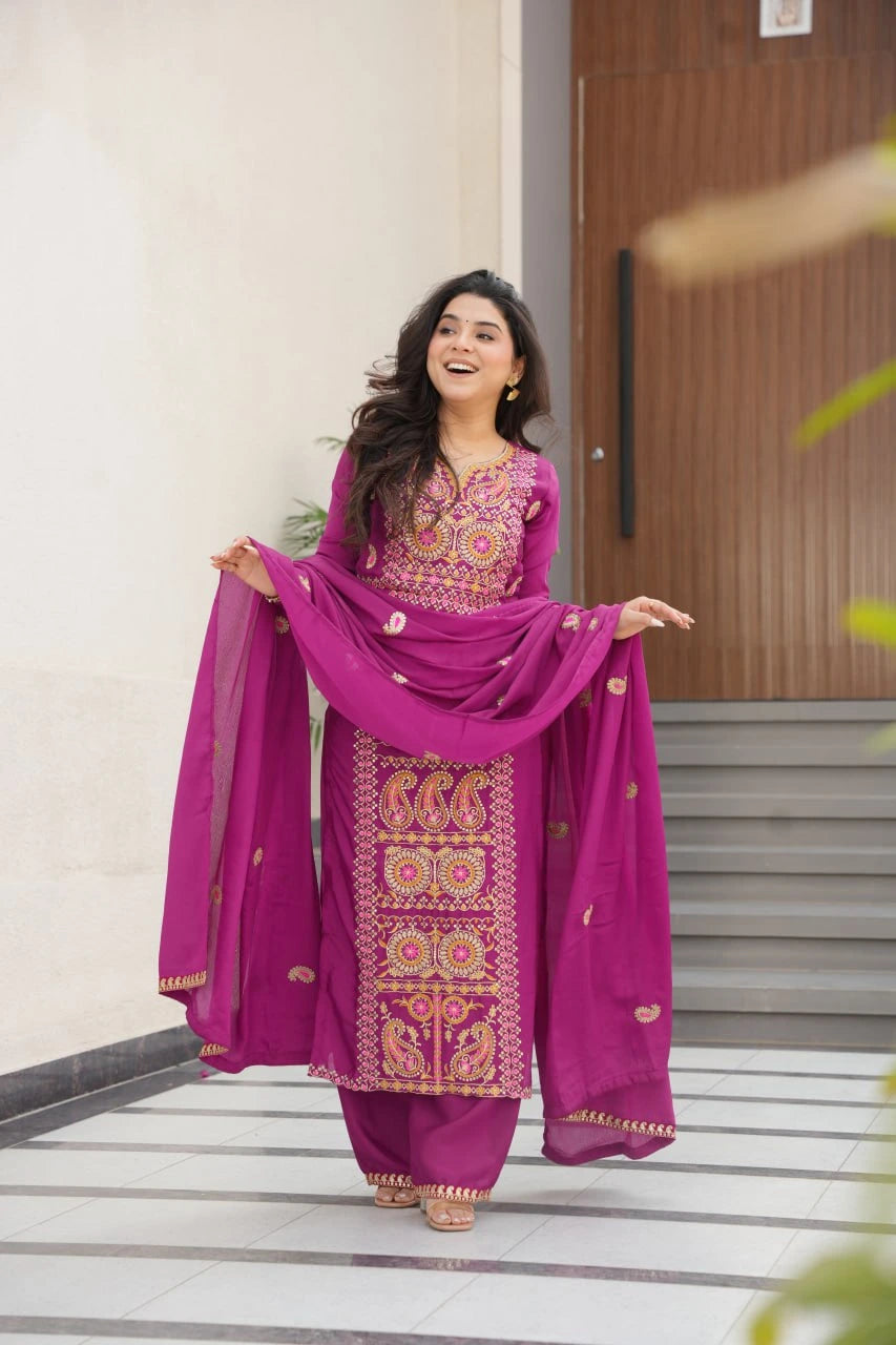 Woman in a vibrant pink traditional outfit with intricate patterns standing on a staircase.