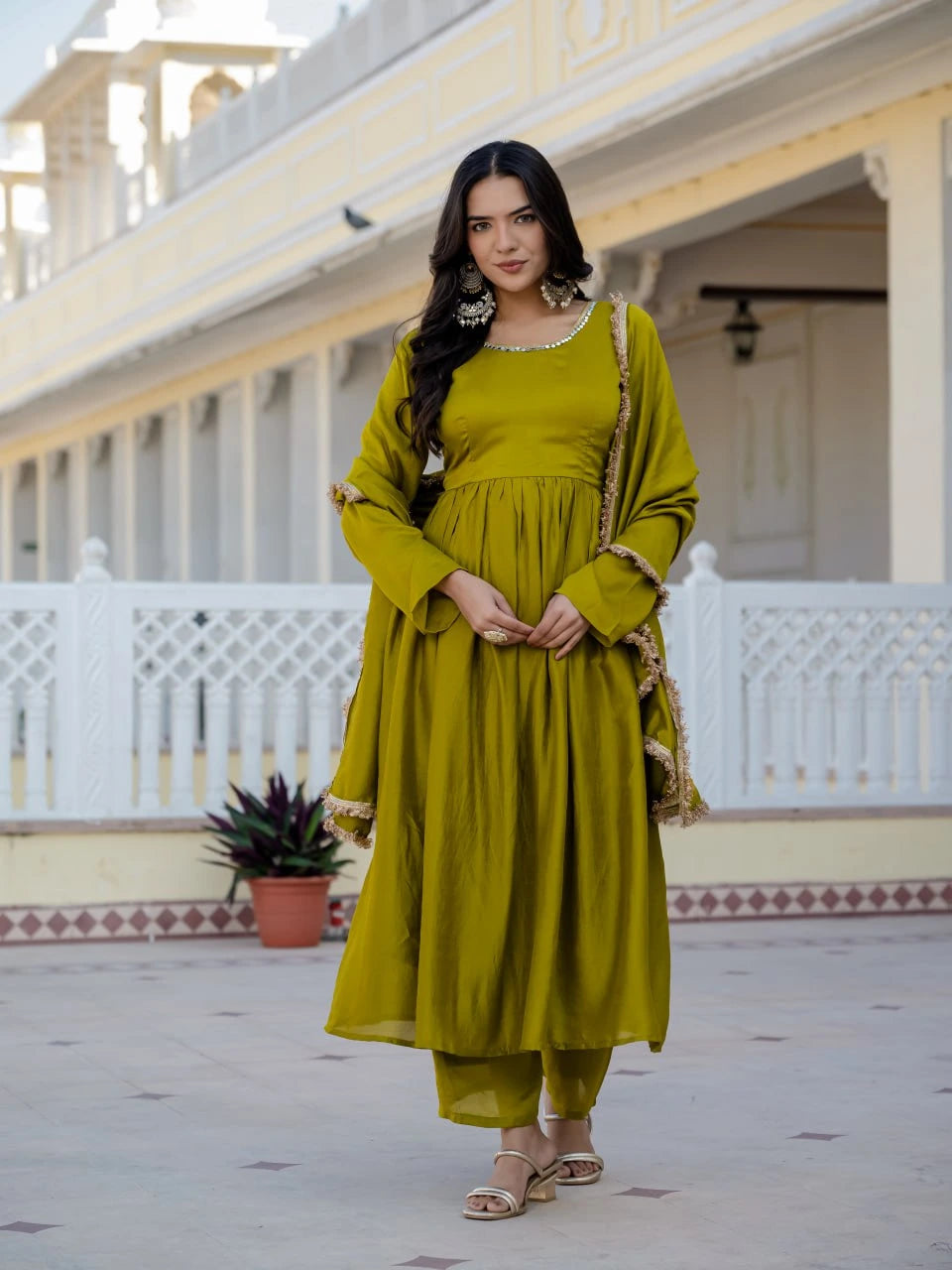 Woman in a green traditional outfit standing in front of a white building with a balcony.