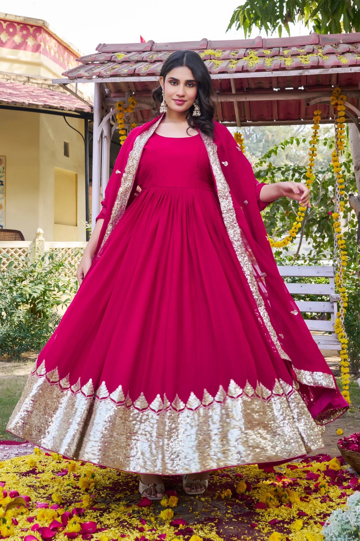 Woman in a pink and gold traditional outfit standing outdoors with greenery in the background