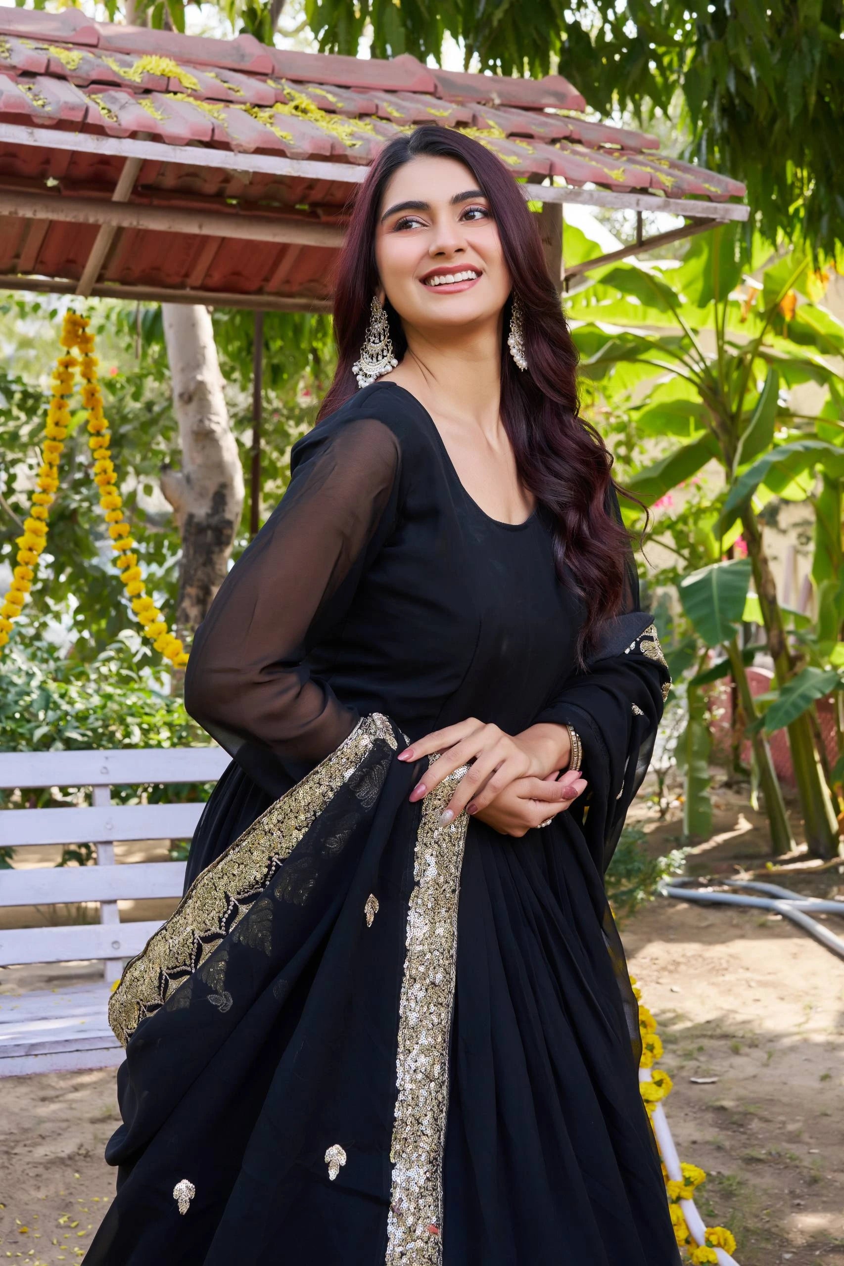 Woman in a black saree with gold details standing outdoors with greenery in the background