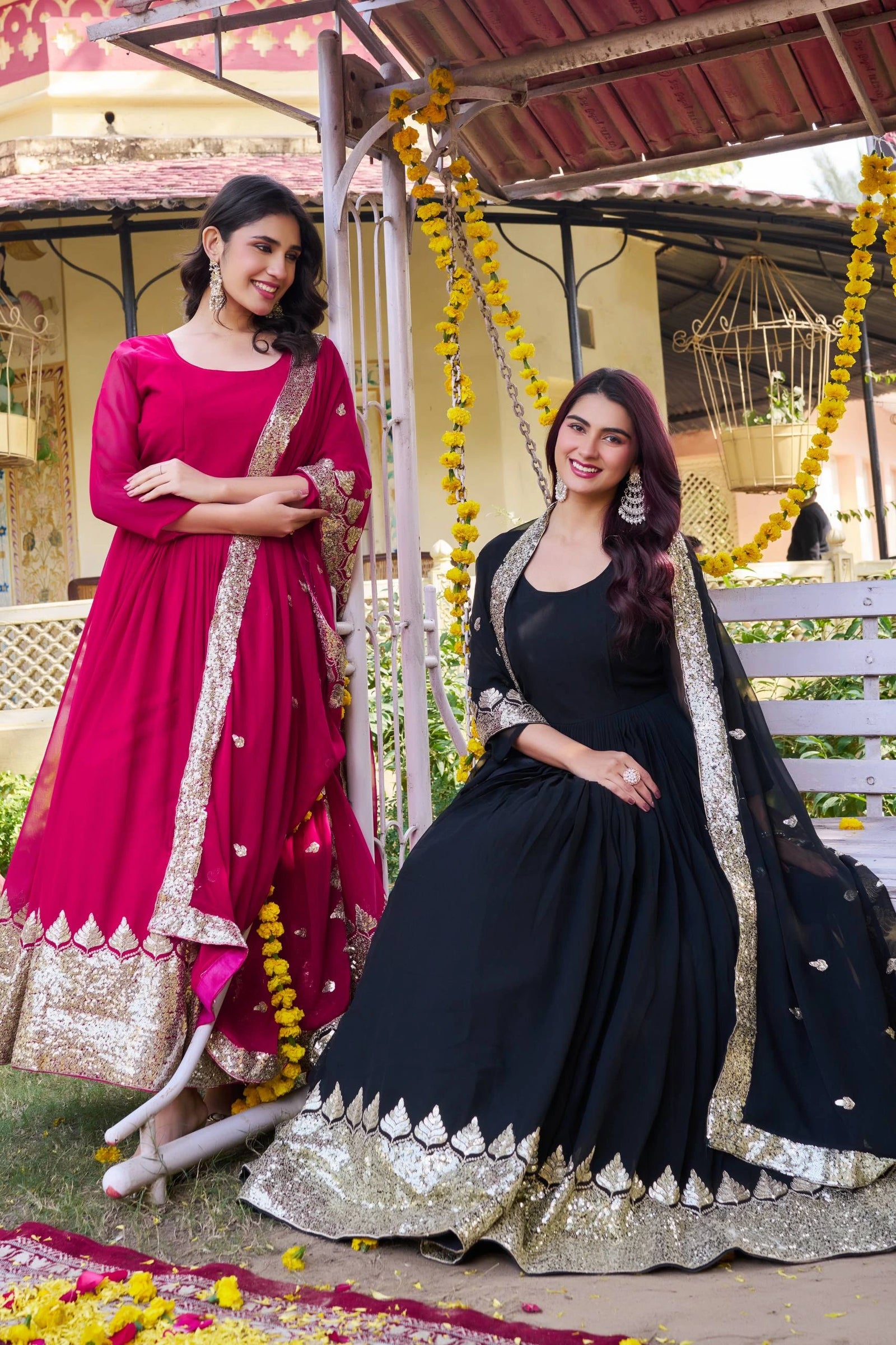 Two women in traditional Indian attire standing on a decorated swing.