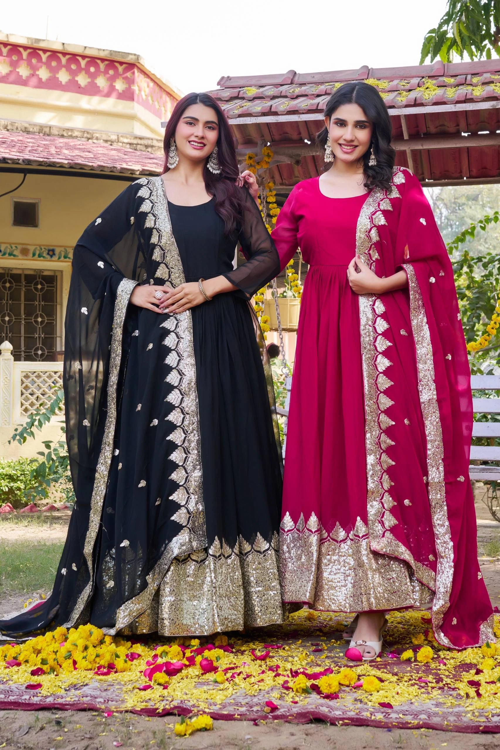 Two women in traditional outfits standing on a decorated ground with flowers.