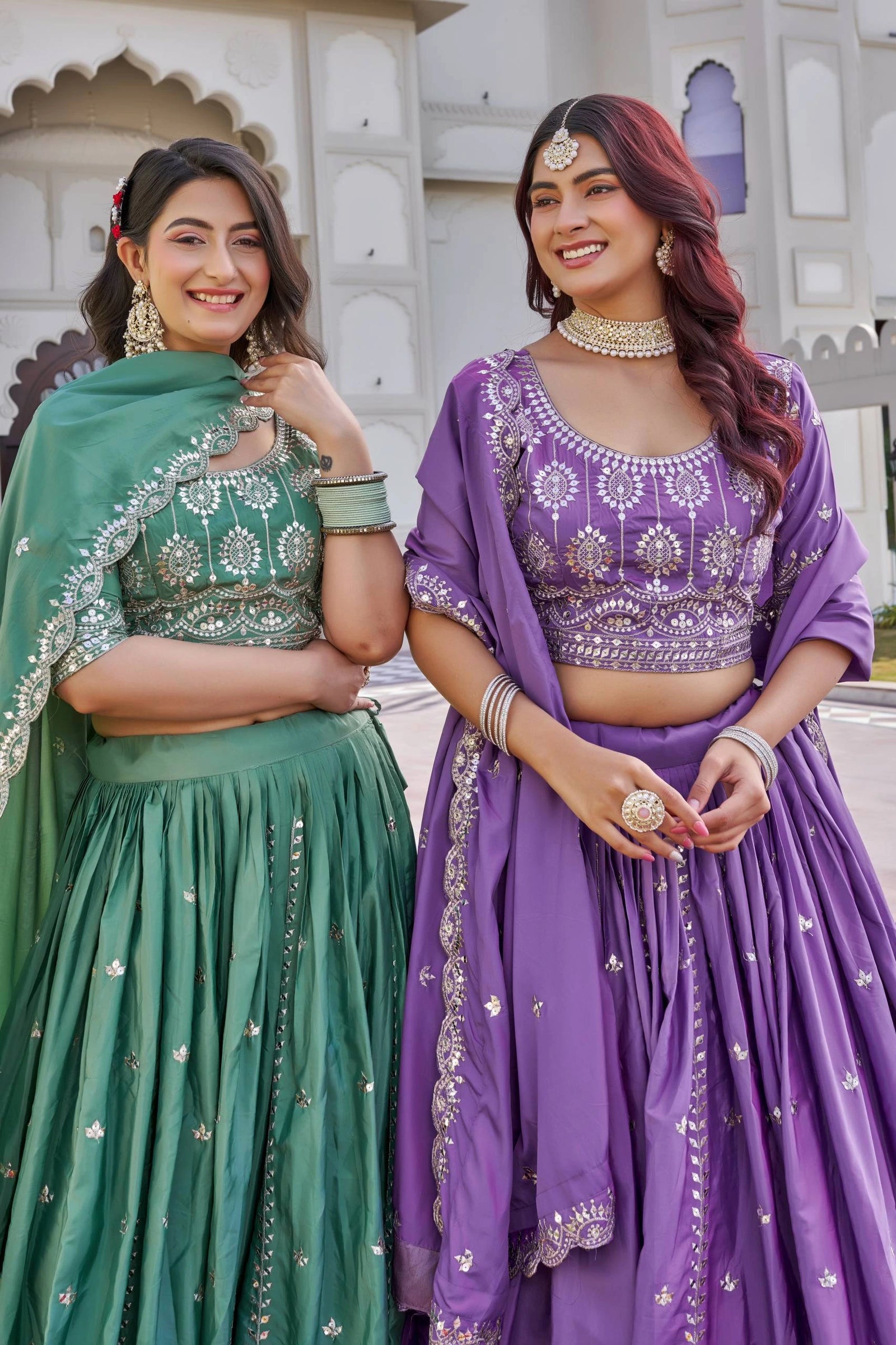 Two women in traditional green and purple dresses standing outdoors.