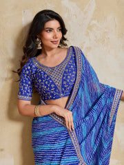 Woman wearing a blue saree with intricate patterns against a beige wall.