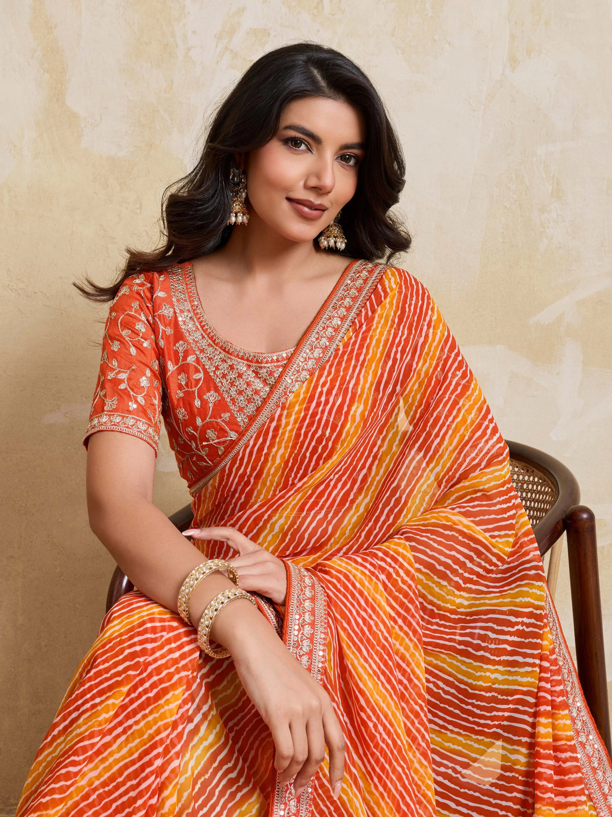 Woman wearing an orange and yellow saree with a beige background