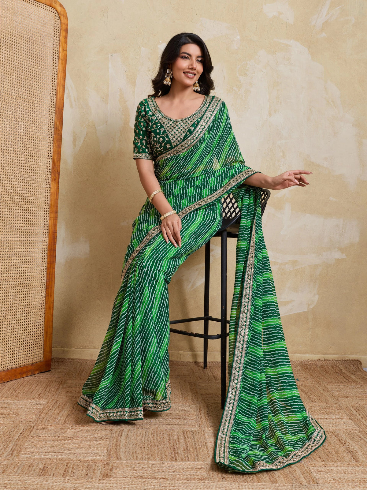 Woman in a green saree with a textured wall and chair in the background