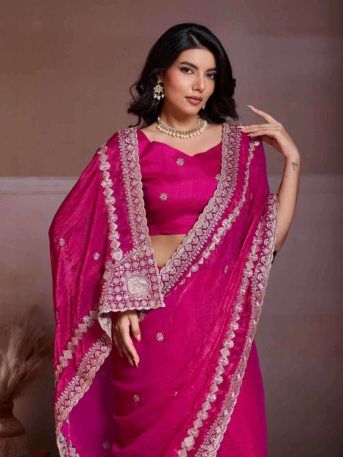 Woman wearing a vibrant pink saree with intricate gold embroidery against a neutral background