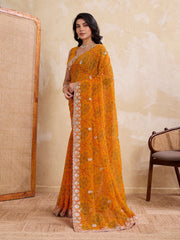 Woman wearing an orange saree with a white border in a room setting.