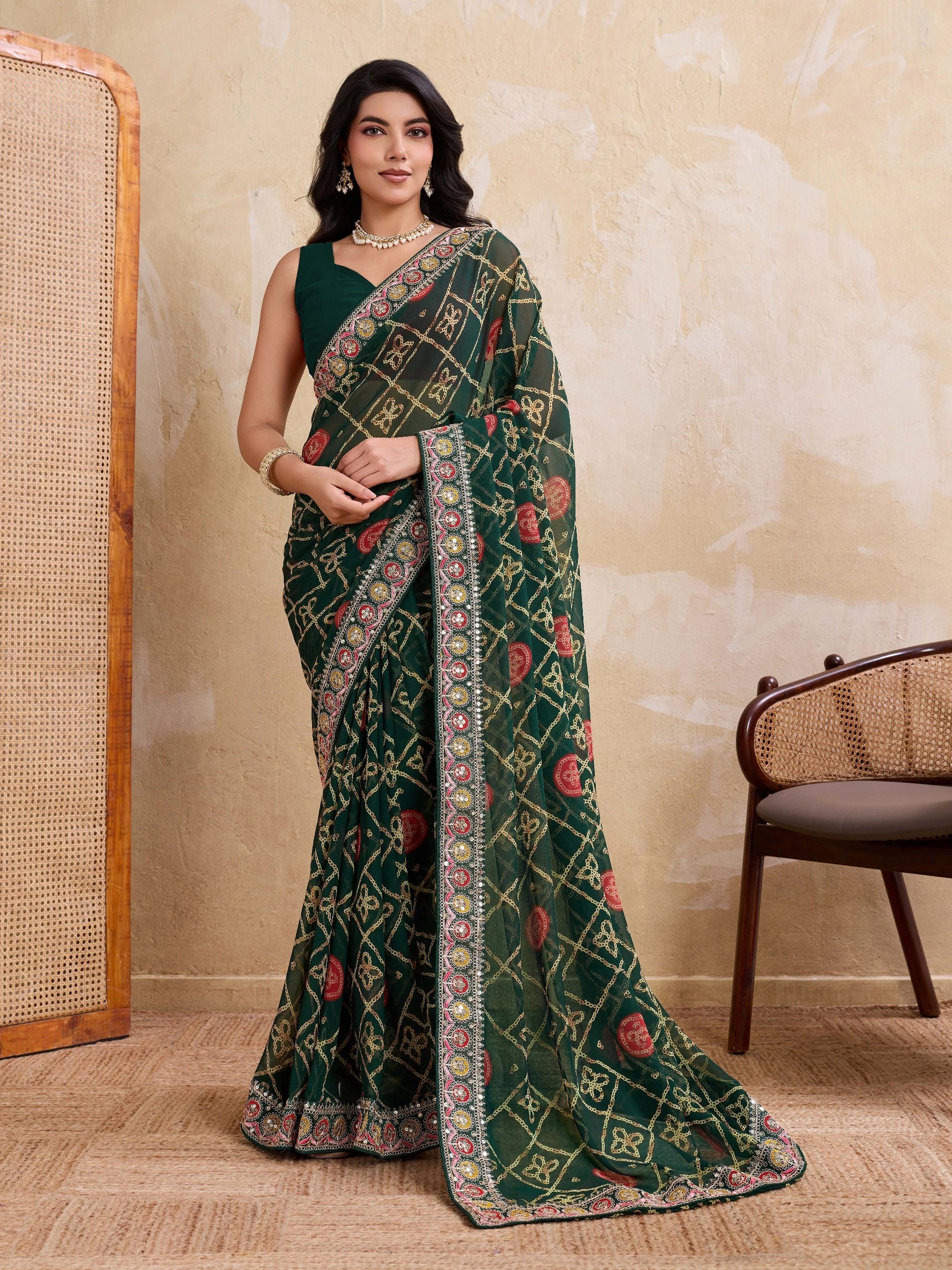 Woman wearing a green saree with intricate patterns in a room with a textured wall and wooden chair.