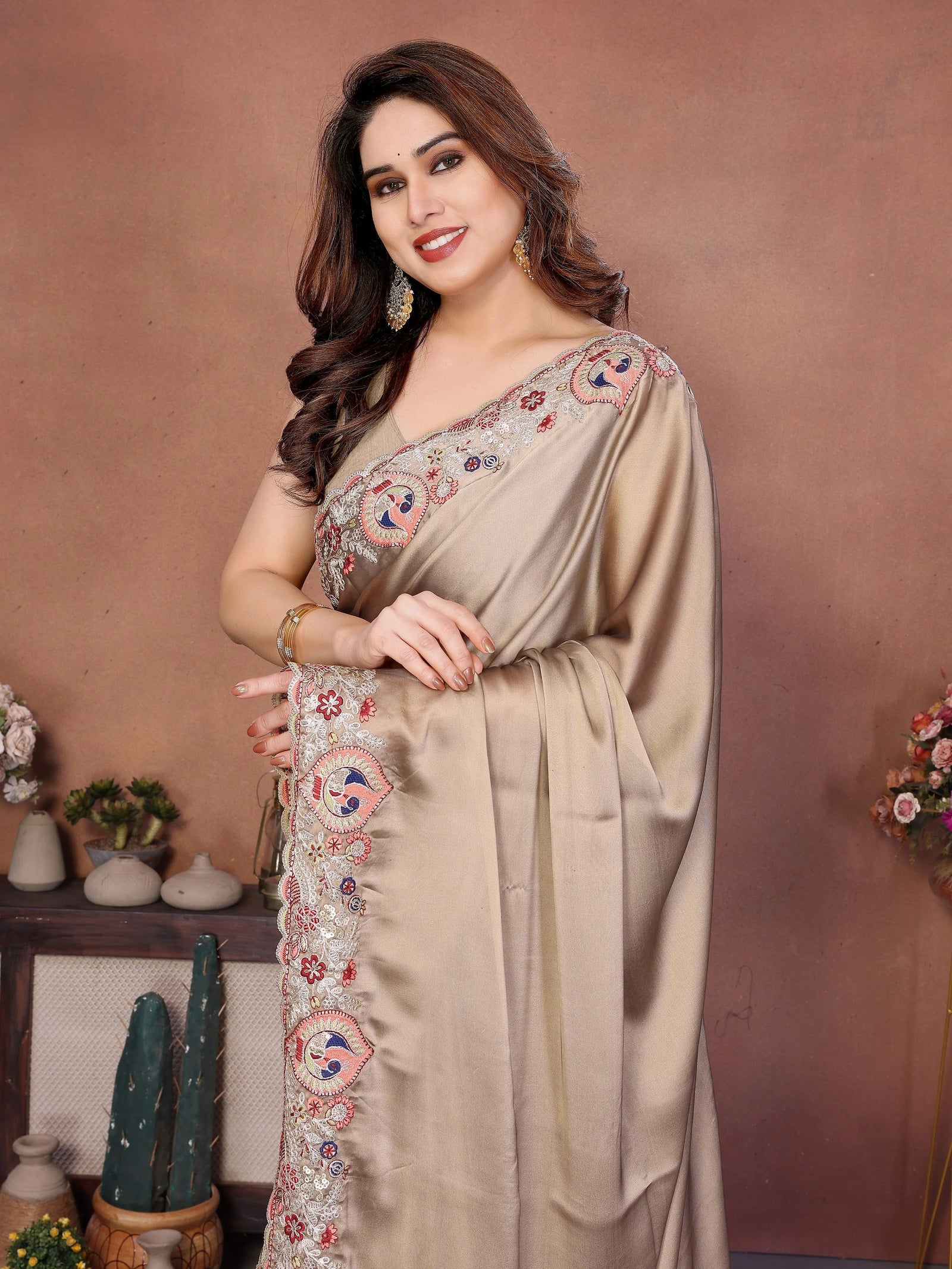 Woman wearing a beige saree with floral embroidery against a brown background
