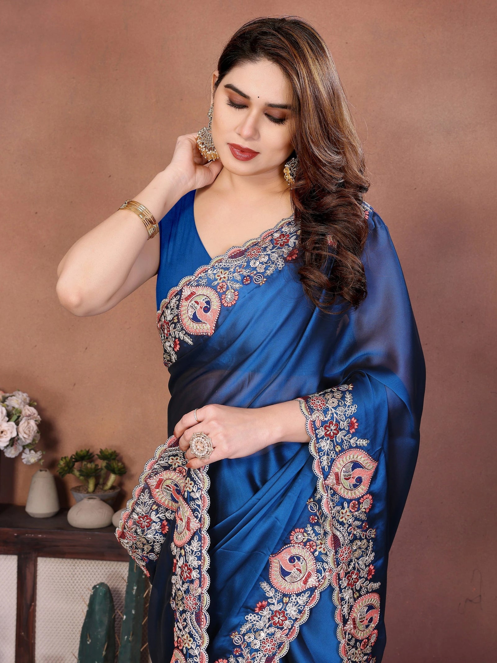 Woman wearing a blue saree with intricate patterns against a brown background