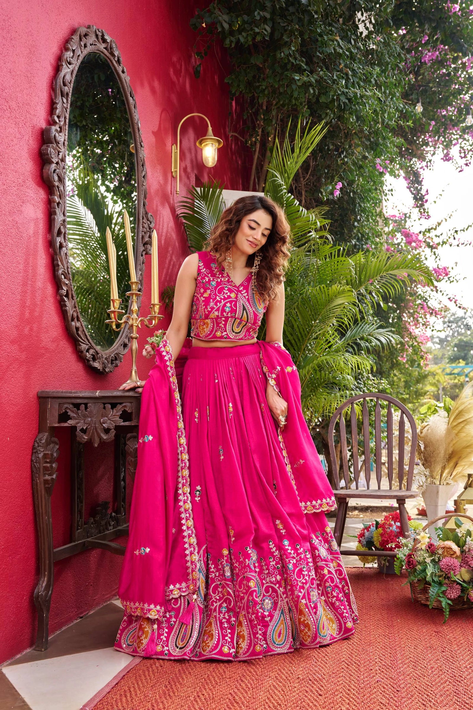 Woman in a bright pink traditional outfit standing in front of a red wall with decorative elements.
