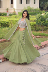 Woman in a green traditional outfit standing outdoors with greenery in the background