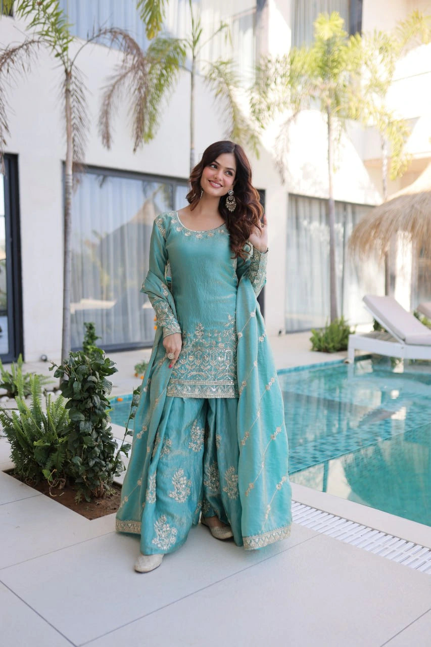 Woman in a teal traditional outfit standing by a pool with a modern building in the background