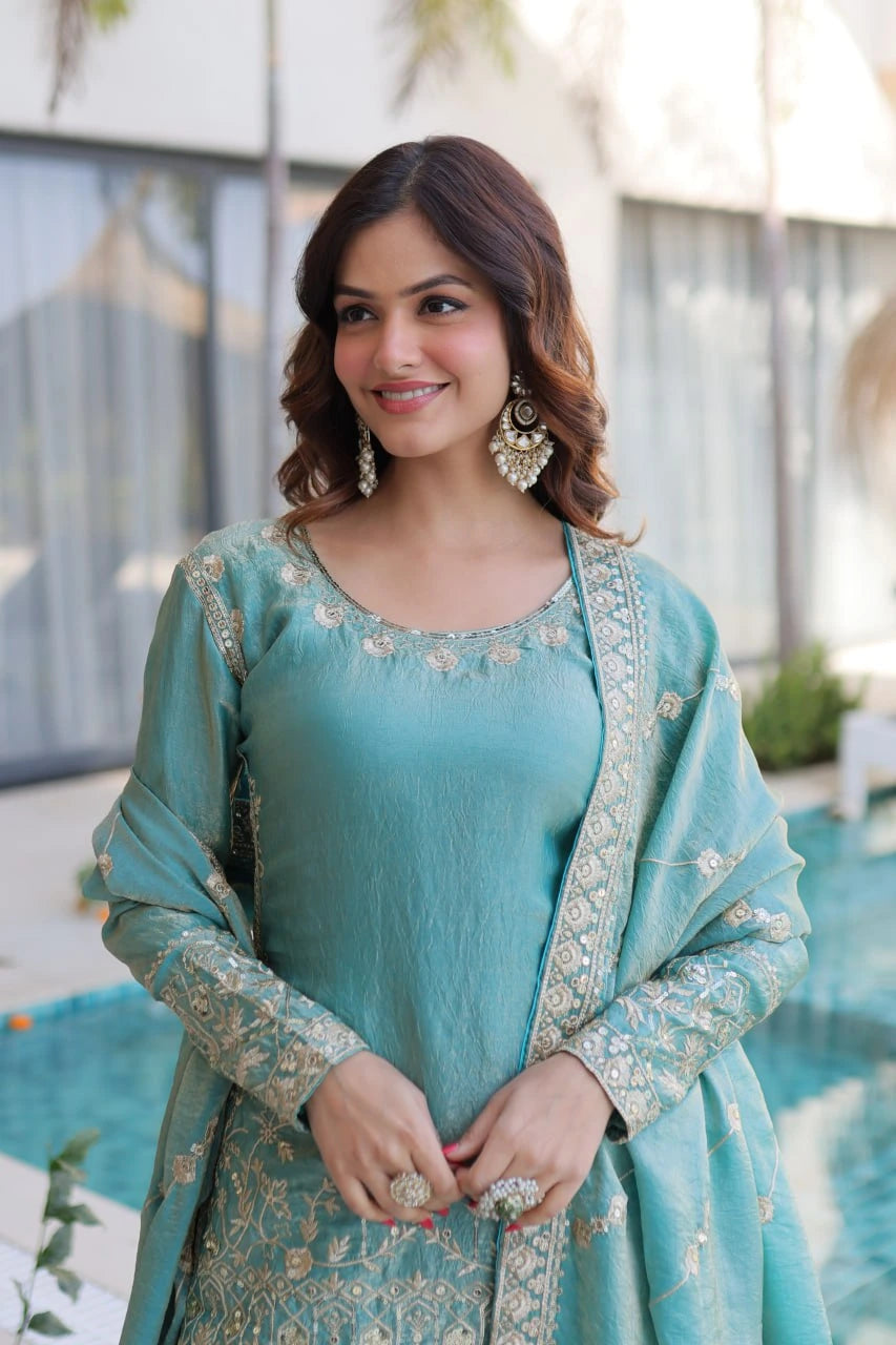Woman wearing a light blue traditional outfit with intricate designs, standing outdoors.